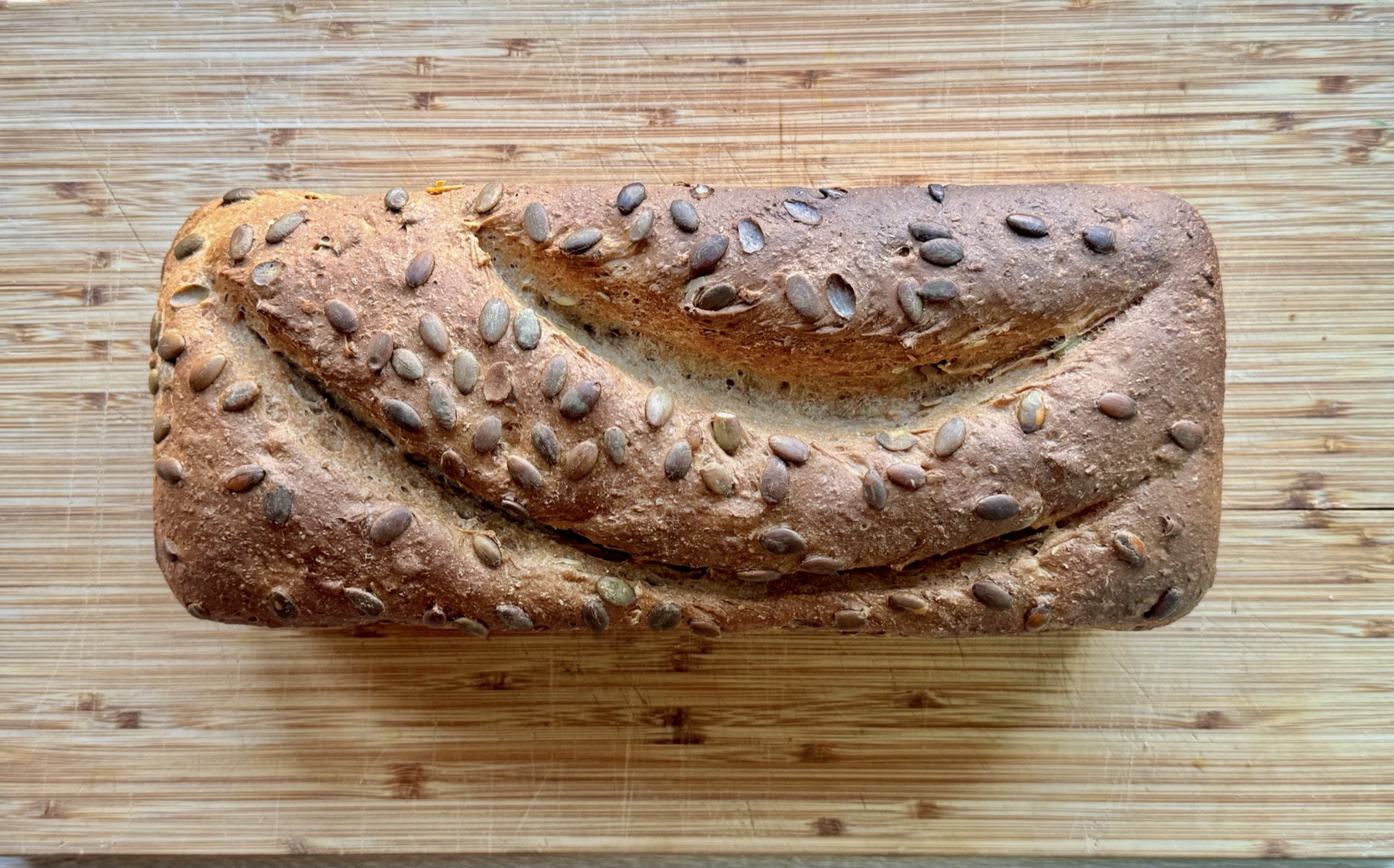 A seeded loaf proving in a tin, dressed with pumpkin and sunflower seeds