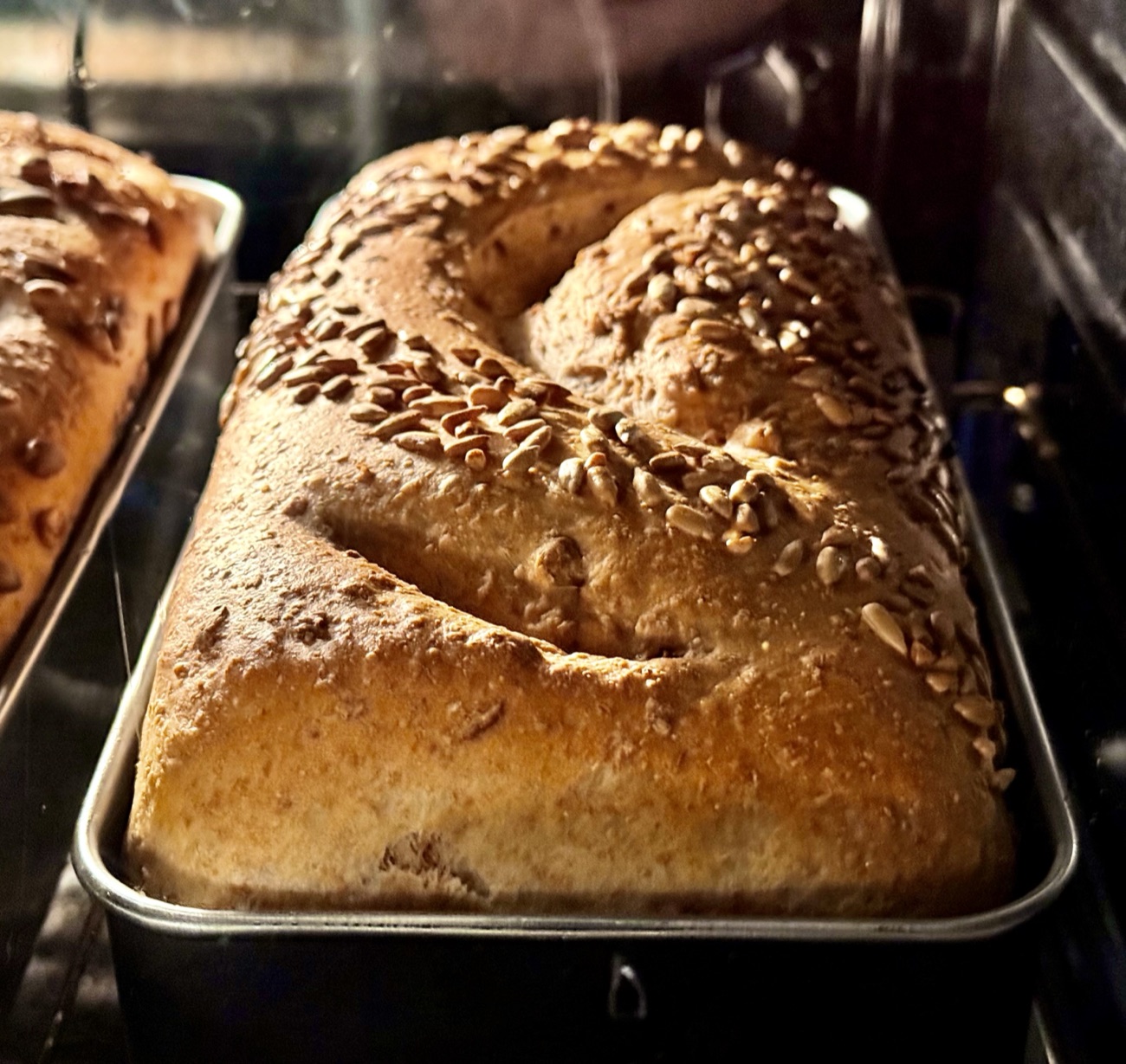 A seeded homemade loaf resting in its baking tin, fresh from the oven